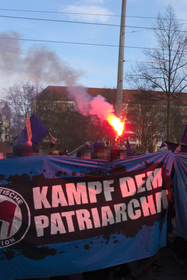 Transparent mit der Aufschrift "Kampf dem Patriarchat", dahinter ein Bengalo